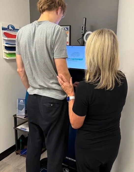 A patient standing on the 3D foot scanner while Dr. Shona checks the results